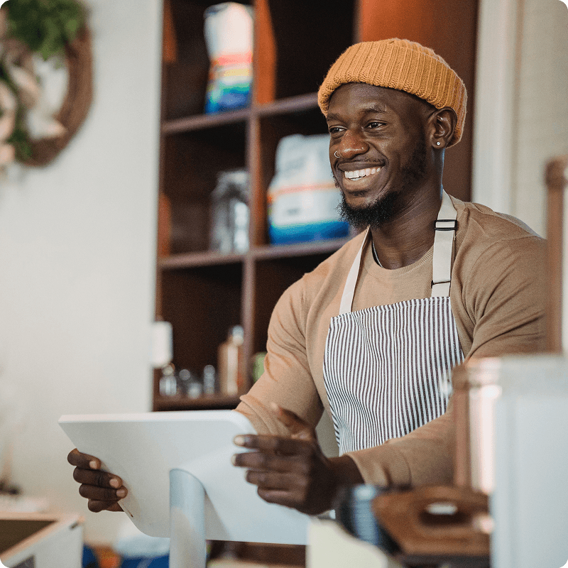Smiling kitchen worker in a beanie and apron holding a tablet